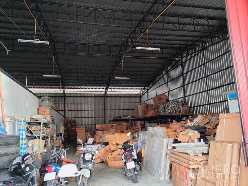 Warehouse for rent in Bang Kapi, Bangkok - High-ceiling steel-frame warehouse interior with shelving, stacked boxes, and overhead lighting.
