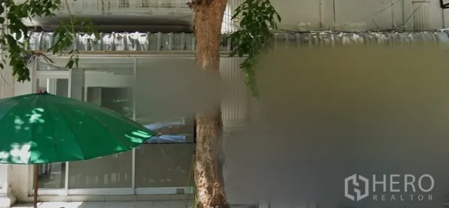 零售空间 出租在Bang Rak, Bangkok - 玻璃推拉门店面，林荫人行道、路边大树与绿色遮阳伞，位于邦拉克商业街。