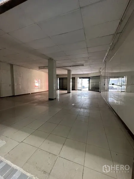 Shophouse for rent in Bang Na, Bangkok - Open-plan retail space with roller shutter frontage and ceiling lights near street entry.