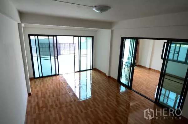 Home Office for rent in Lat Phrao, Bangkok - Open‑plan ground floor with glossy wood‑look tiles and large sliding glass partitions.