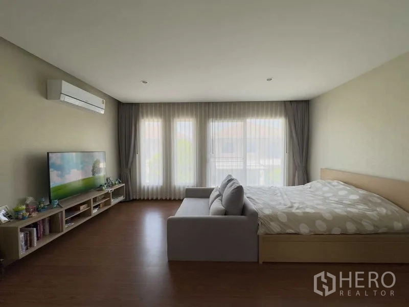 Detached House for rent or sale in Bang Khen, Bangkok - Spacious master bedroom with floor-to-ceiling windows, sofa, TV unit and wood floors.