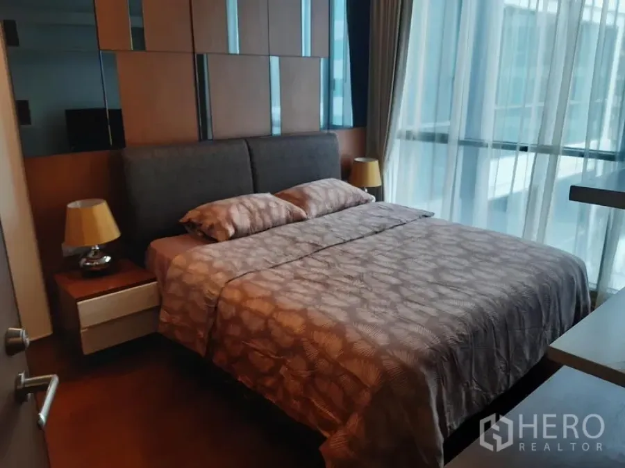 Condominium for rent in Watthana, Bangkok - Cozy bedroom with upholstered headboard, bedside tables, and floor-to-ceiling windows with sheer curtains.