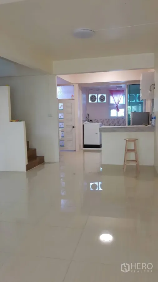 Townhouse for rent in Khlong Toei, Bangkok - Open-plan living area with glossy tile floors, staircase, and a view into the compact kitchen with breakfast bar.
