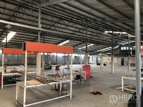 Warehouse for rent or sale in Khlong Luang, Pathum Thani - Spacious warehouse floor with steel trusses, worktables, and high ceilings.