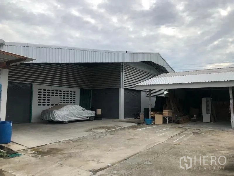 Warehouse for rent in Mueang Pathum Thani, Pathum Thani - Metal-clad warehouse exterior with roller shutter doors, covered loading bay, and a large concrete yard for truck access and parking.
