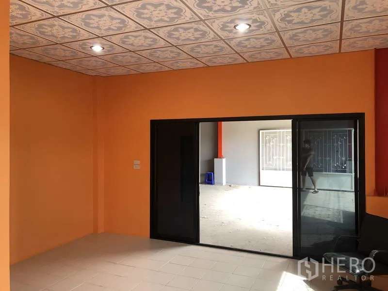 Warehouse for rent in Nonthaburi - Ground-floor office with orange walls, patterned ceiling tiles and black sliding glass doors opening to the warehouse.