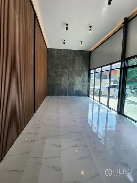 Warehouse for rent in Lam Luk Ka, Pathum Thani - Ground-floor showroom with marble tiles, stone accent wall and full-height windows.