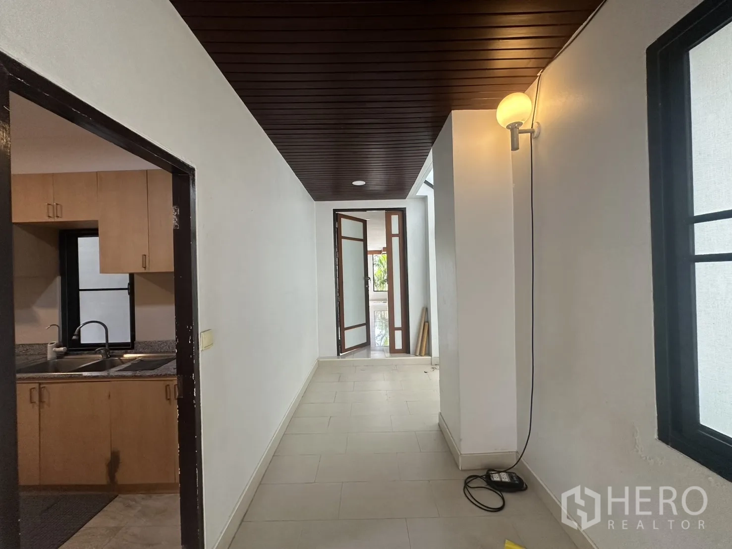Detached House for rent in Watthana, Bangkok - Hallway with dark wood ceiling beside the kitchen, leading to glass doors.