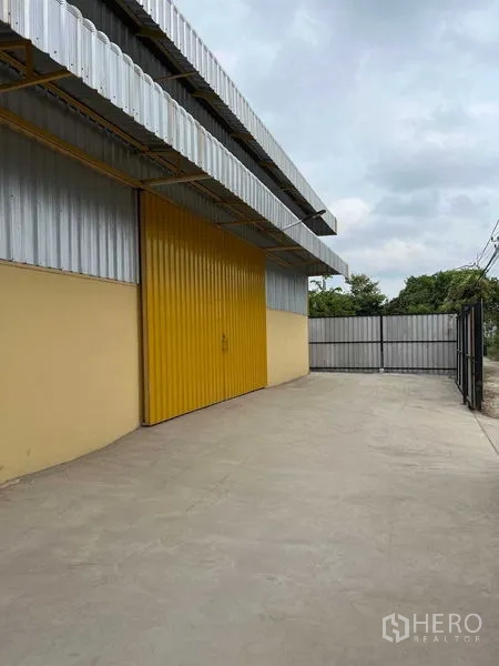 Warehouse for rent in Lat Krabang, Bangkok - Exterior of warehouse showing wide yellow metal loading door, concrete apron, and fenced gate.