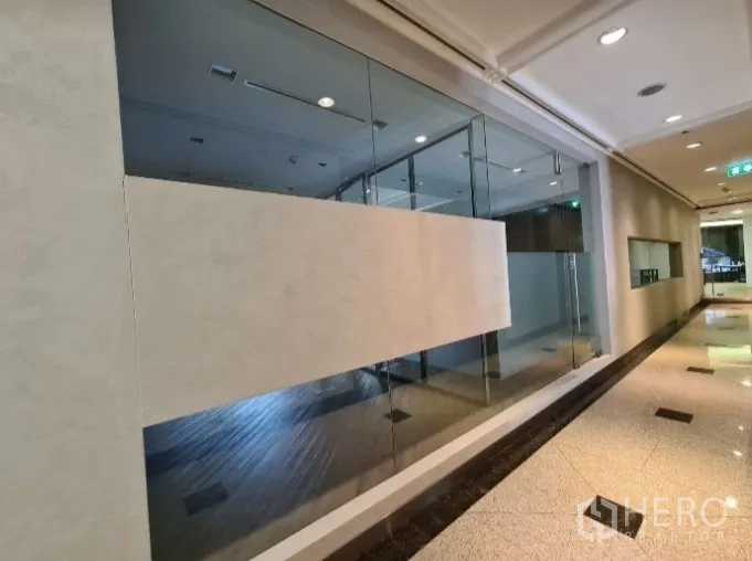 Office Space for rent - Building corridor facing a glass-walled office frontage.