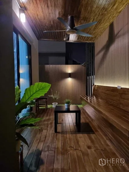 Detached House for sale in Khan Na Yao, Bangkok - Covered wooden terrace with ceiling fan, long bench seating and potted plants in warm lighting.