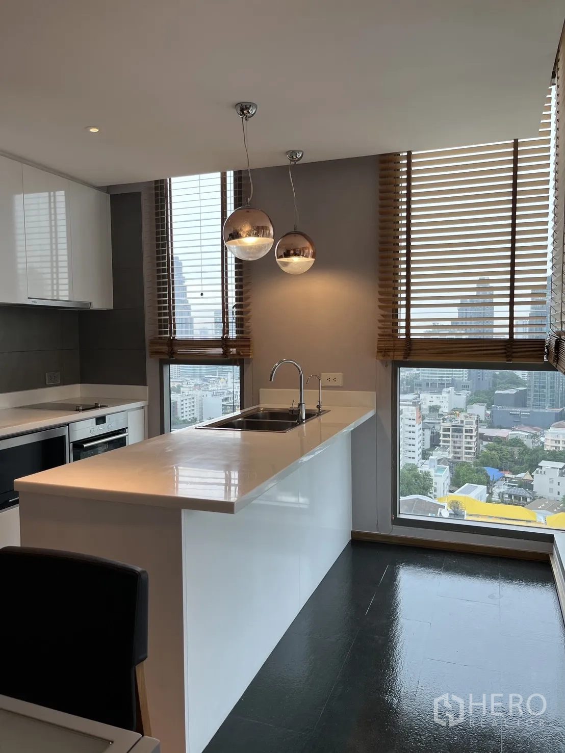 Condominium for rent in Watthana, Bangkok - Sleek white kitchen with long countertop and large corner windows overlooking the city.