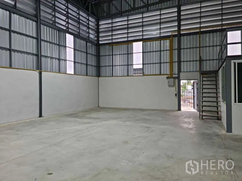 Warehouse for rent in Bang Bua Thong, Nonthaburi - Open warehouse space with stairs to mezzanine, high truss roof and concrete flooring.
