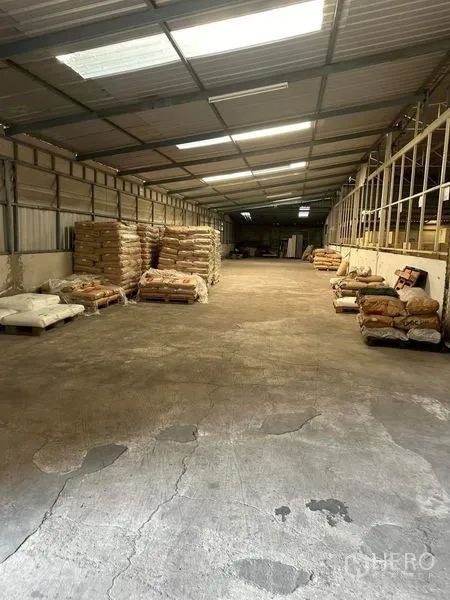 货栈 出租在Yan Nawa, Bangkok - 宽敞储存大厅，两侧堆放托盘与袋装货物，金属屋顶下。