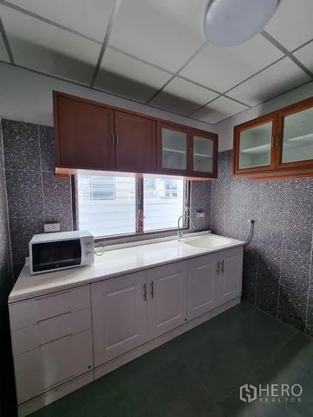 Detached House for rent in Nonthaburi - Kitchen close-up showing storage cabinets, sink, and natural light.