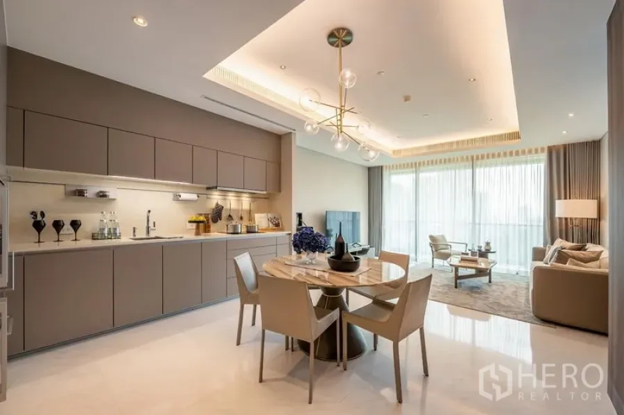 Condominium for rent or sale in Pathum Wan, Bangkok - Contemporary kitchen with full-height cabinets beside dining table and light-filled lounge.