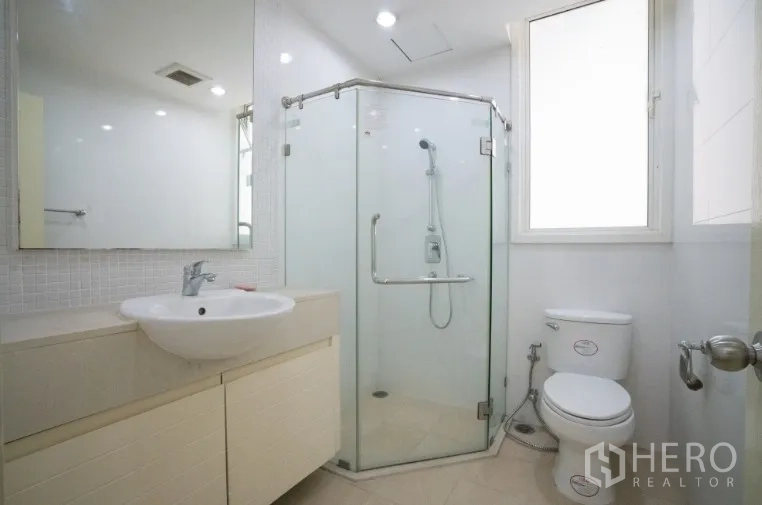 Condominium for rent or sale in Khlong Toei, Bangkok - Second bathroom with corner glass shower, window and white vanity.
