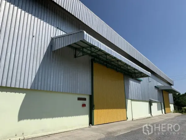 Warehouse for rent in Lat Krabang, Bangkok - Metal-clad warehouse exterior with a wide yellow sliding door and loading canopy under a clear blue sky.