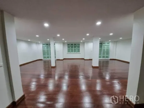 Shophouse for rent in Bang Rak, Bangkok - Spacious open-plan interior with polished dark wood floors, white walls, recessed LED lights, pillars and large windows in a Pathum Wan shophouse.
