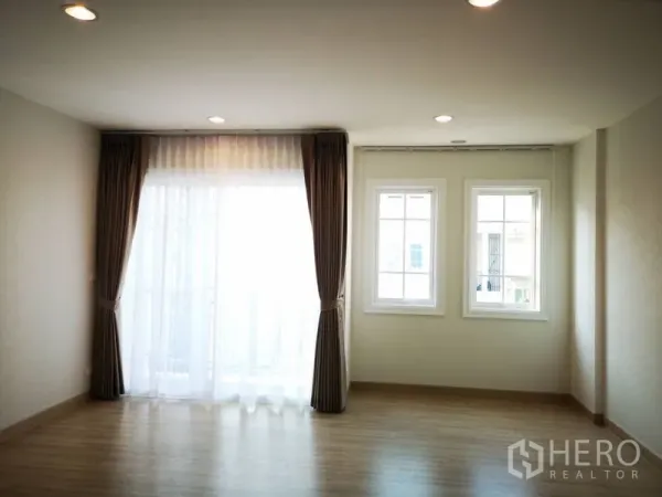 Townhouse for rent in Bang Na, Bangkok - Bright upper-floor bedroom with recessed lighting, two windows and balcony access