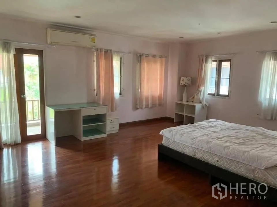 Townhouse for rent in Watthana, Bangkok - Bedroom with bed, desk, balcony door and several curtained windows.
