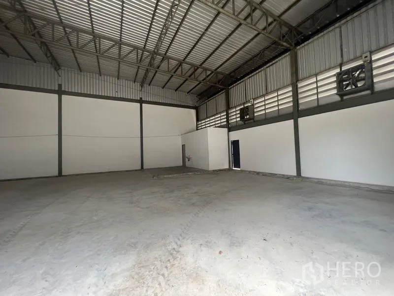 Warehouse for rent or sale in Sai Noi, Nonthaburi - Interior shot showing ventilation fans, clear-span roof and small service sink.