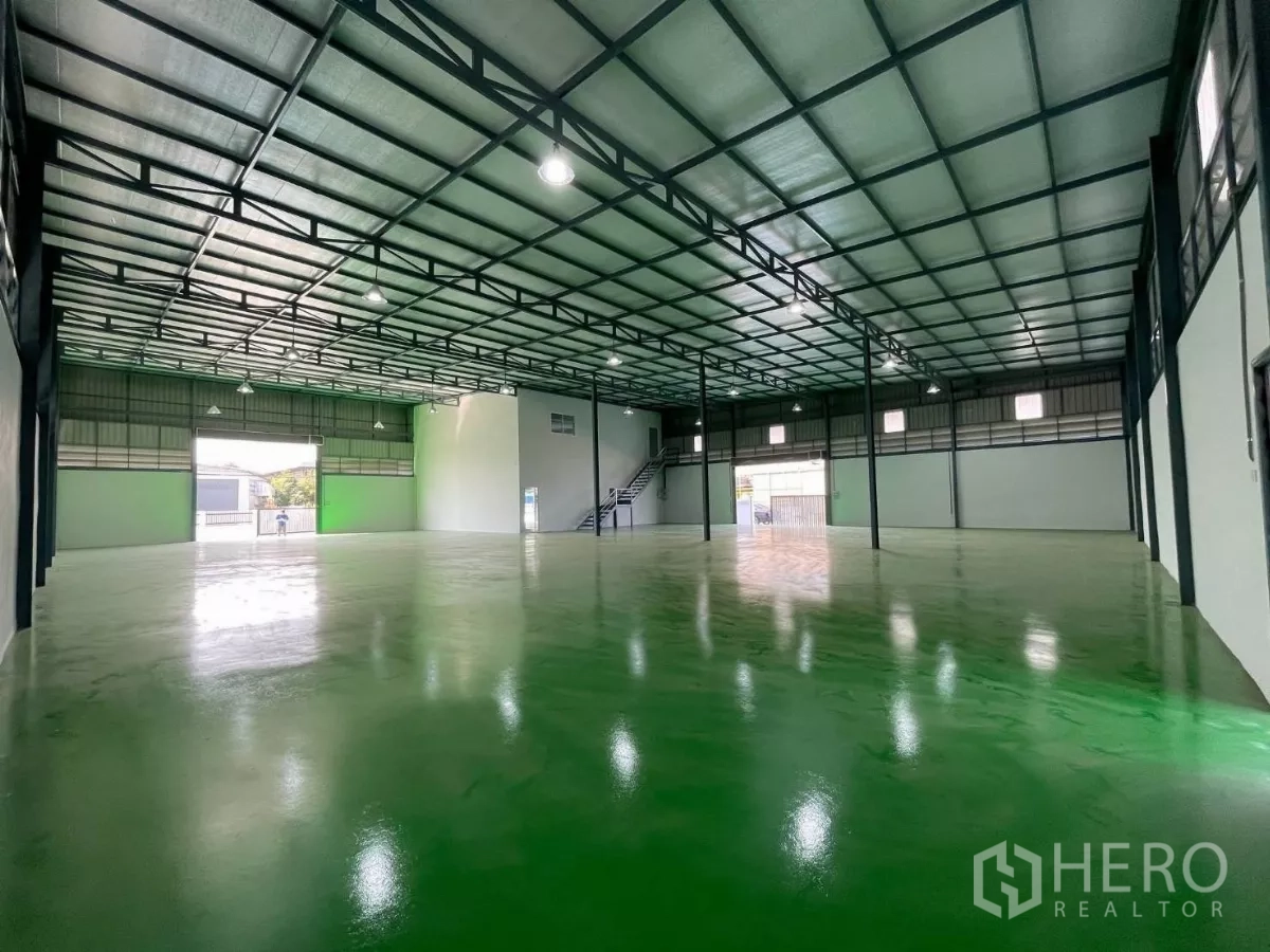 Factory for rent or sale in Bang Phli, Samut Prakan - Spacious warehouse interior with steel truss roof, bright lighting, roller shutter doors, and glossy heavy-duty green floor.