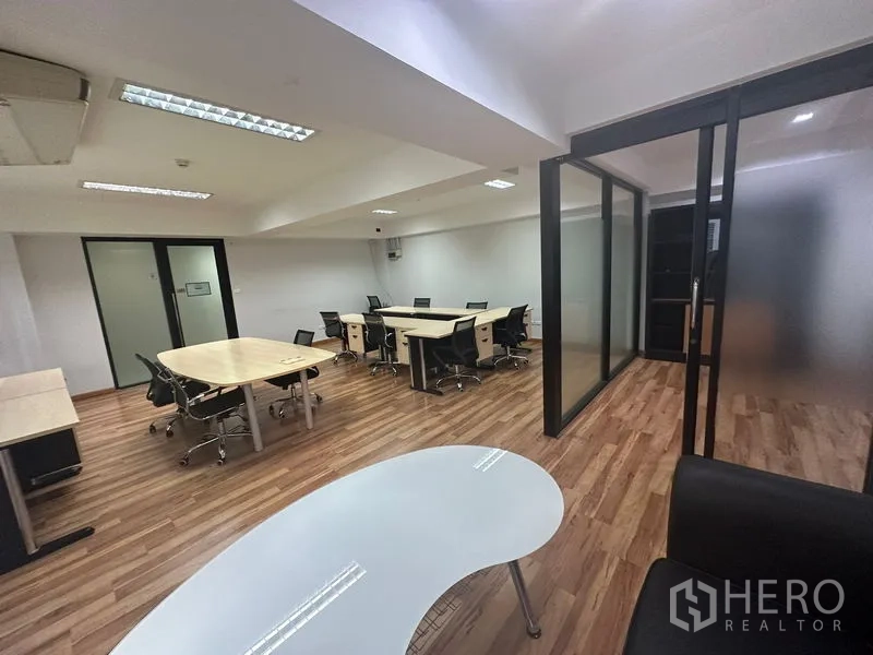Office Space for rent in Khlong Toei, Bangkok - Workspace view showing multiple desks, sliding glass doors with frosted panels, and a lounge table on wood flooring.