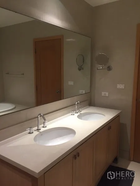 Condominium for rent in Khlong Toei, Bangkok - Bathroom vanity with a large mirror and double sinks on a light countertop.