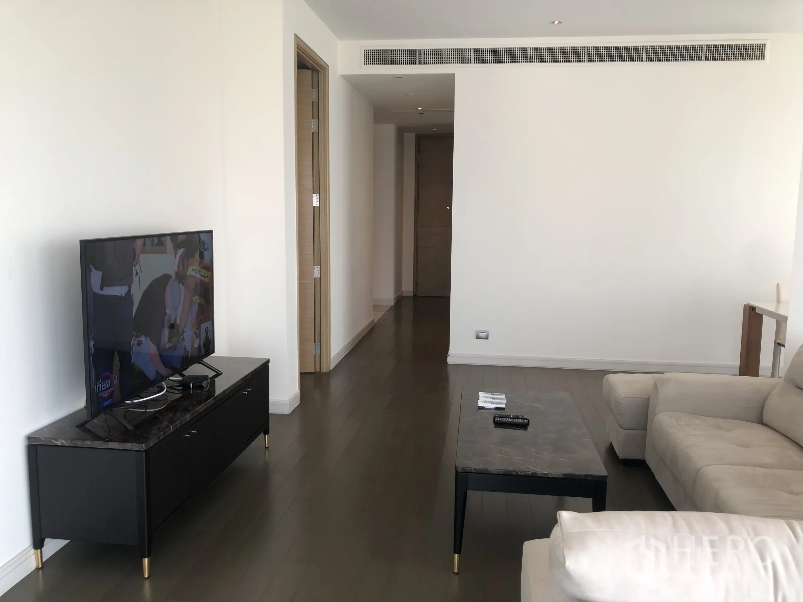 Condominium for rent in Pathum Wan, Bangkok - Spacious lounge showing TV stand, marble-top table, hallway entrance and wood flooring.