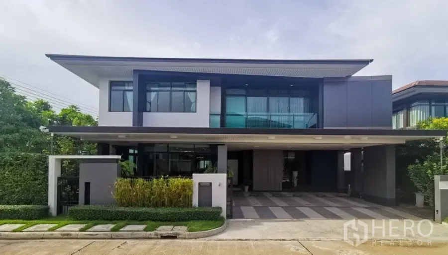 Detached House for rent or sale in Bang Kapi, Bangkok - Modern two-storey detached house with wide covered carport, landscaped hedges, and large windows.