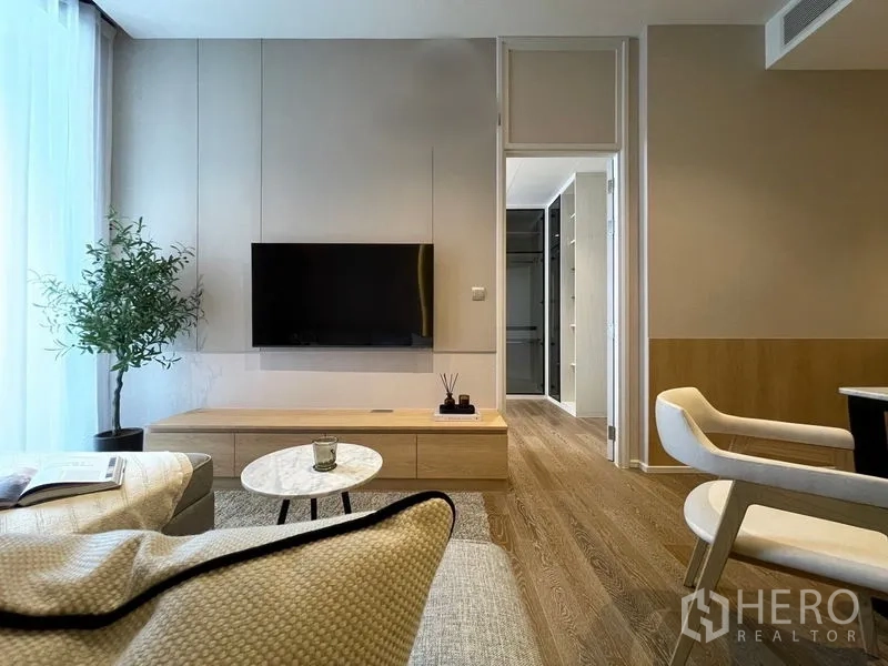 Condominium for rent or sale in Pathum Wan, Bangkok - Living area with wall-mounted TV, low console, doorway to closet, wood floors and balcony light.