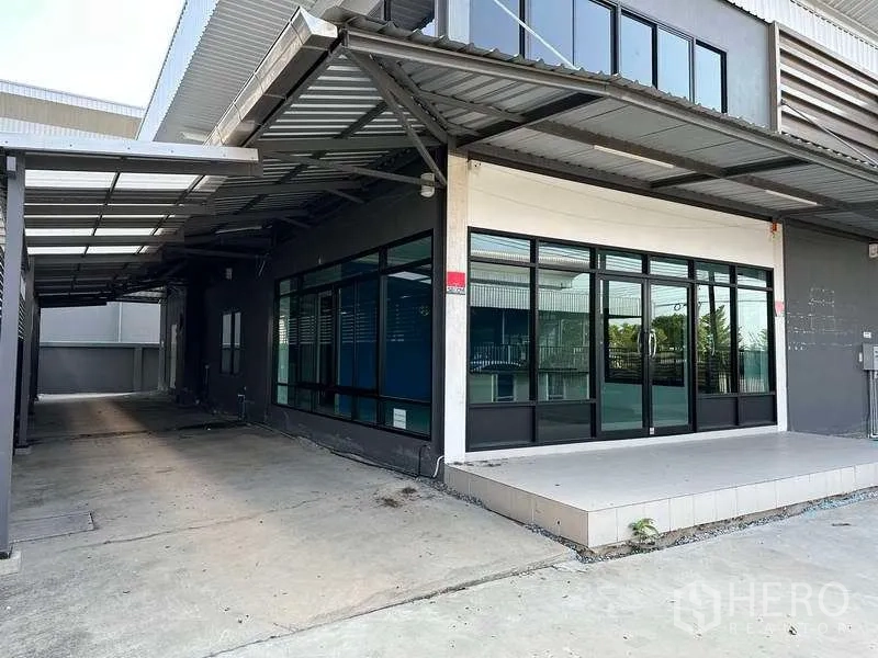 Factory for rent in Samut Prakan - Covered side walkway and glass entrance under a metal canopy.