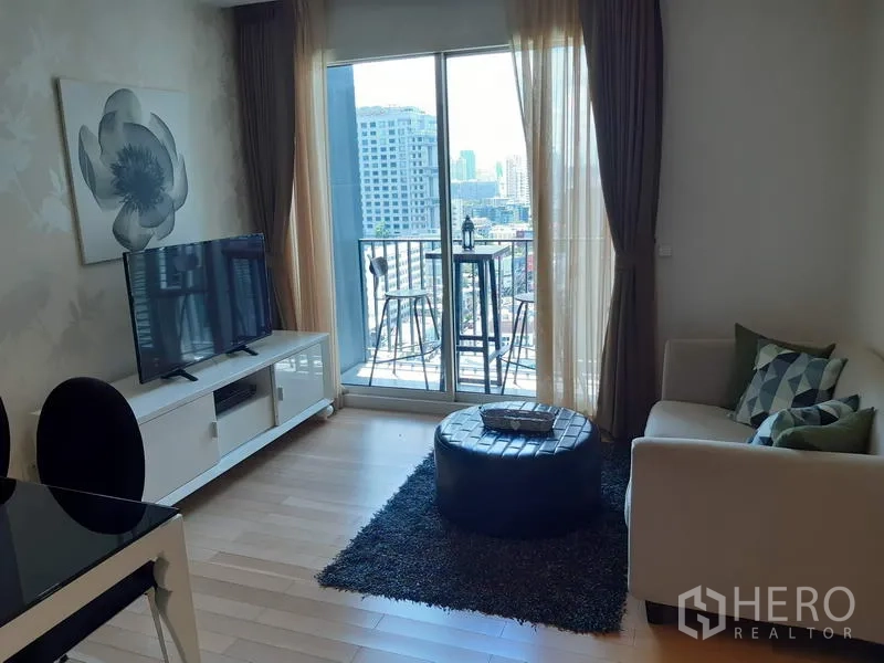Condominium for rent in Khlong Toei, Bangkok - Bright living room with sofa, TV console and sliding doors opening to a balcony with city view.