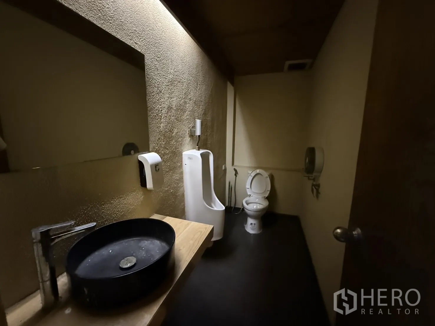 Detached House for rent in Watthana, Bangkok - Restroom with urinal, toilet and black basin under warm lighting.