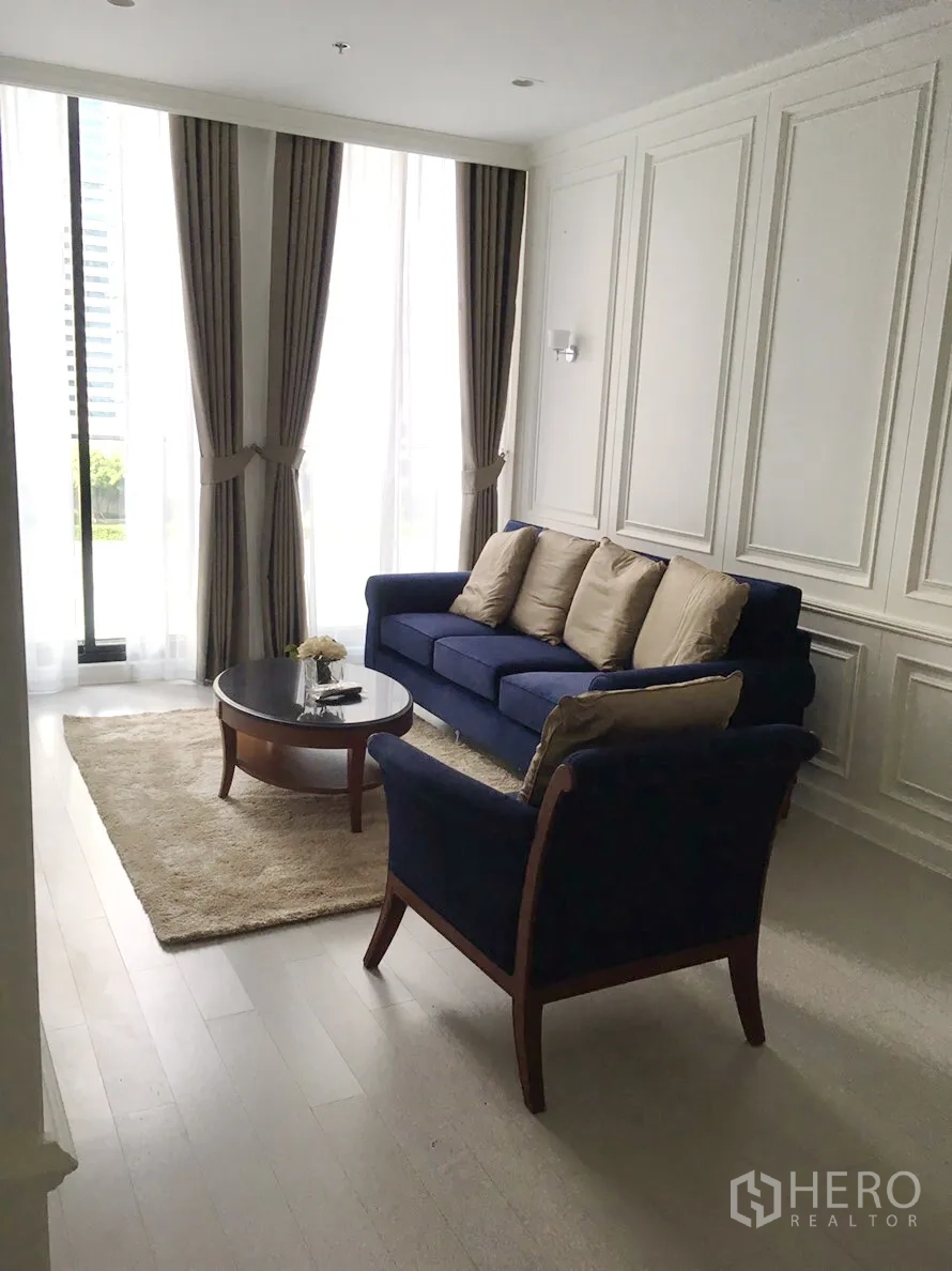 Condominium for rent in Pathum Wan, Bangkok - Bright living room with navy sofa set, paneled walls, and floor-to-ceiling curtains.