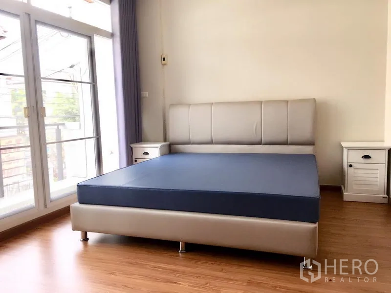 Townhouse for rent in Prawet, Bangkok - A master bedroom with large windows, balcony doors and matching bedside tables.