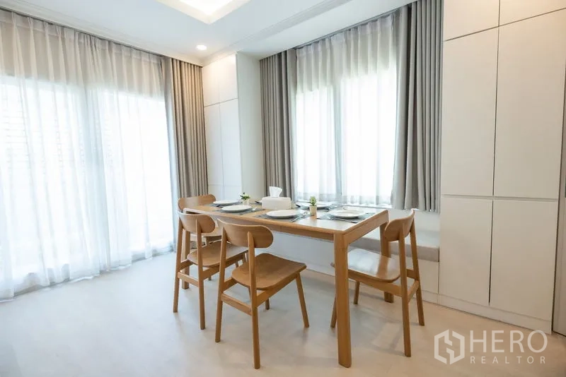 Detached House for rent or sale in Bang Phli, Samut Prakan - Dining area with wooden table for four beside full-height windows and storage.