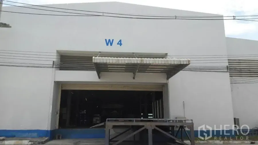 工厂 出租在Chachoengsao - 白色工厂外观，卷闸门与带雨棚的装卸平台，标有 W4。