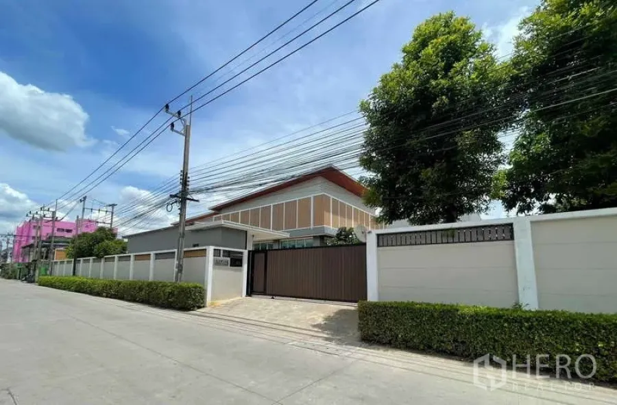 Factory for sale in Krathum Baen, Samut Sakhon - Street view of a gated industrial property with a high perimeter wall and trees.