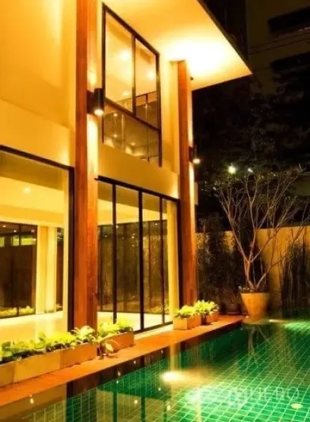 บ้าน ให้เช่าในKhlong Toei, Bangkok - มุมใกล้ของตัวบ้านริมสระ กระจกสูง เสาไม้ และไฟโทนอุ่น