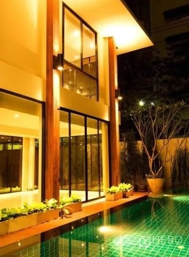 บ้าน ให้เช่าในKhlong Toei, Bangkok - มุมใกล้ของตัวบ้านริมสระ กระจกสูง เสาไม้ และไฟโทนอุ่น