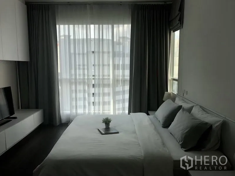 Condominium for rent in Pathum Wan, Bangkok - Bright bedroom with floor-to-ceiling windows, sheer drapes, TV console, and a king bed with neutral linens.