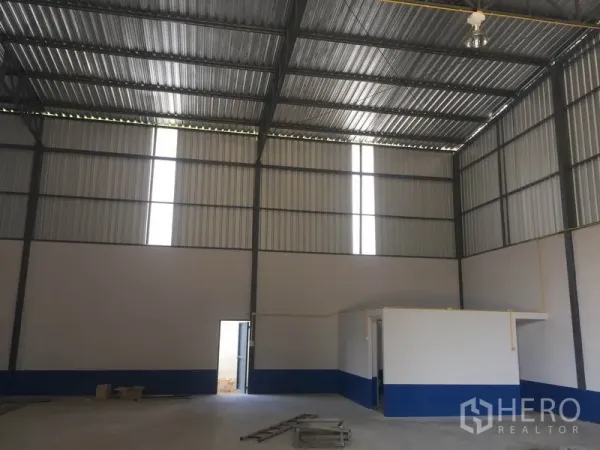 Warehouse for rent in Sai Mai, Bangkok - High-ceiling warehouse interior with steel frame, white-and-blue walls, skylight panels and a small office room.