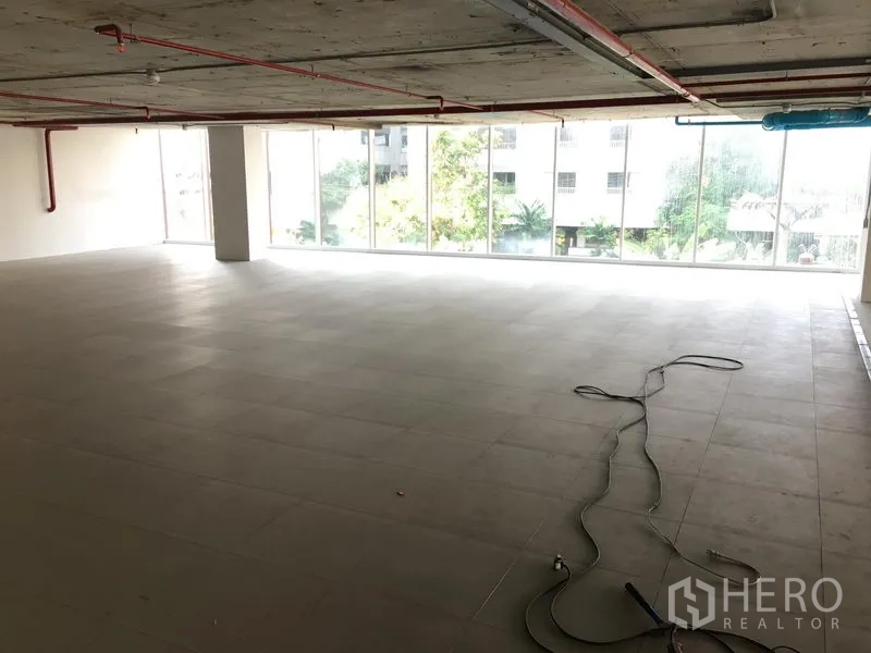 Retail Space for rent in Khlong Toei, Bangkok - Spacious shop floor with unfinished ceiling, floor-to-ceiling windows, and natural light overlooking greenery.