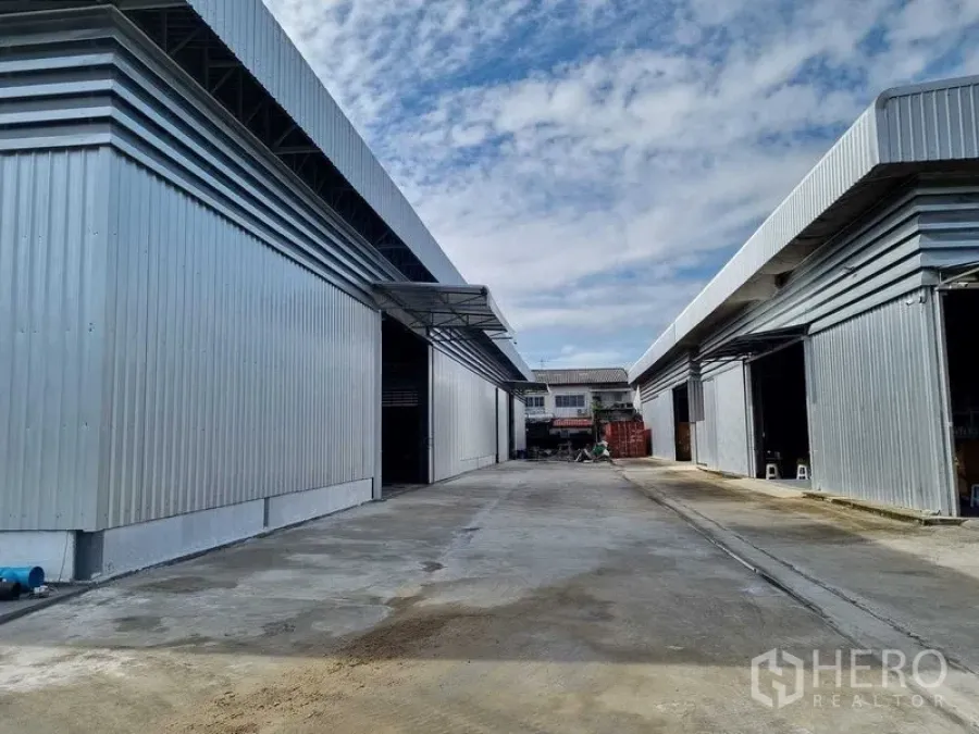 Warehouse for rent in Khlong Sam Wa, Bangkok - Exterior of modern steel-clad warehouse buildings with wide driveway and multiple roll-up doors.