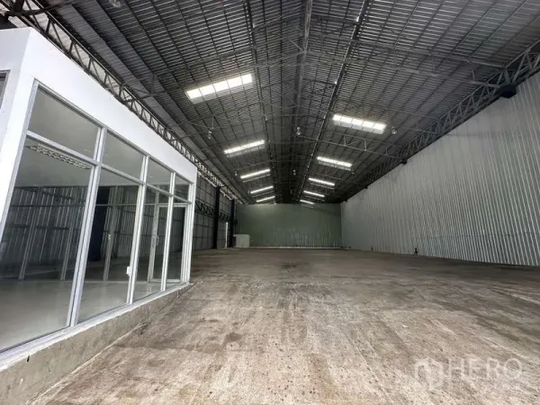 Warehouse for rent in Pak Kret, Nonthaburi - High-clearance warehouse hall with bright lighting, concrete floor, and side office.
