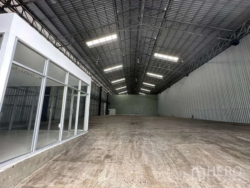 Warehouse for rent in Pak Kret, Nonthaburi - High-clearance warehouse hall with bright lighting, concrete floor, and side office.