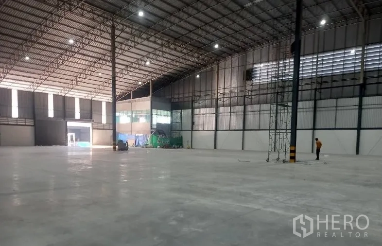 Factory for rent in Si Racha, Chon Buri - Open warehouse floor with tall columns and a corner office with windows.