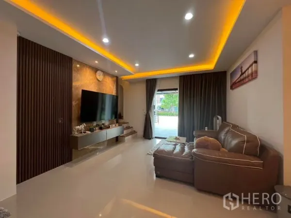 Townhouse for rent - Living room with leather sofa, TV feature wall, cove lighting and sliding door to the front.